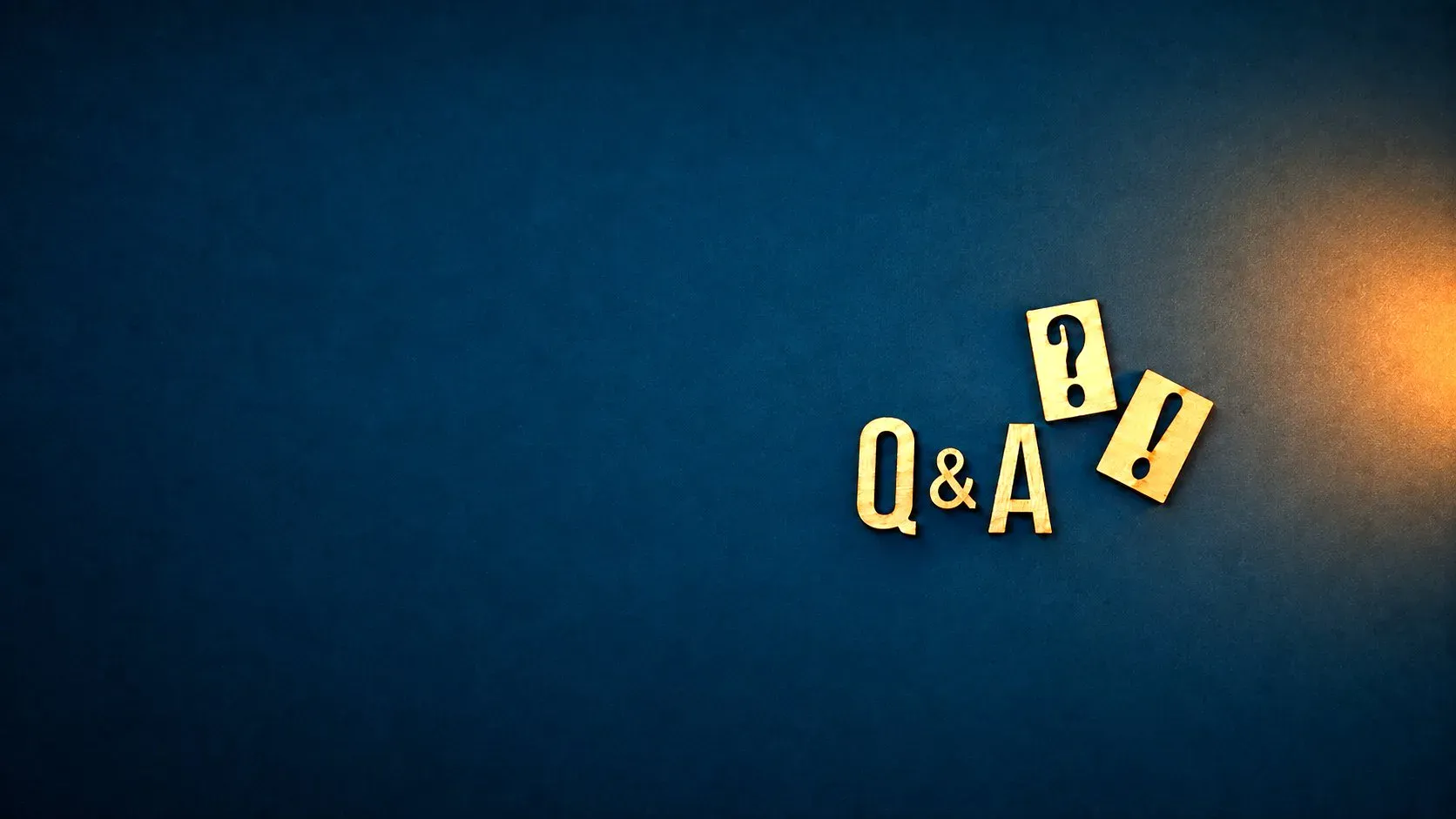 Wooden letters spelling Q and A beside a question mark and an exclamation mark, lit from the right on dark blue