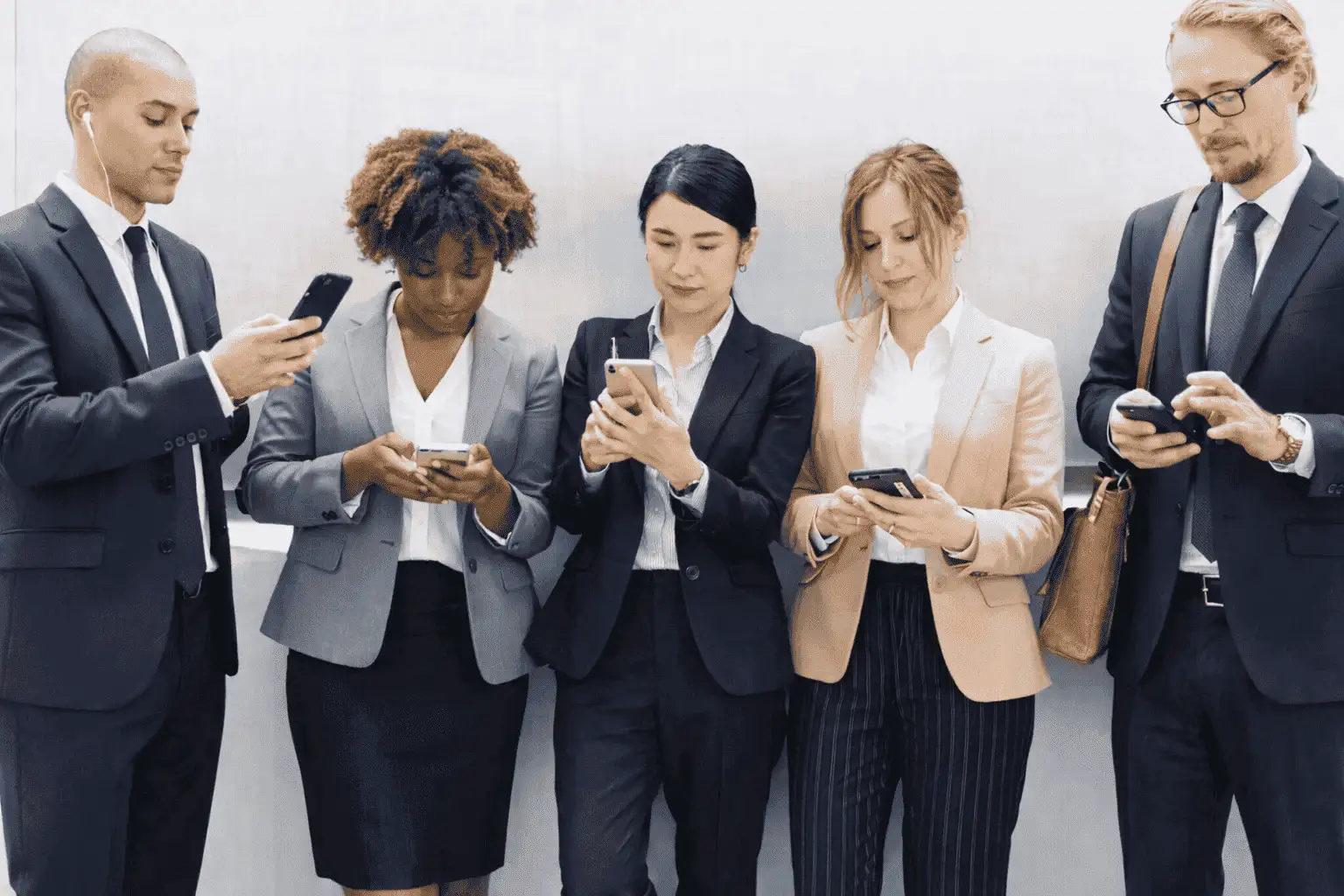 Five colleagues standing side by side against a pale wall, each looking down at their own phone